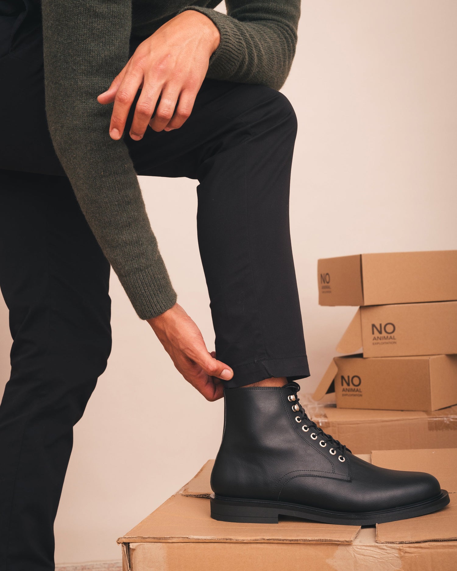 Person wearing black boots sitting on cardboard boxes with a neutral background