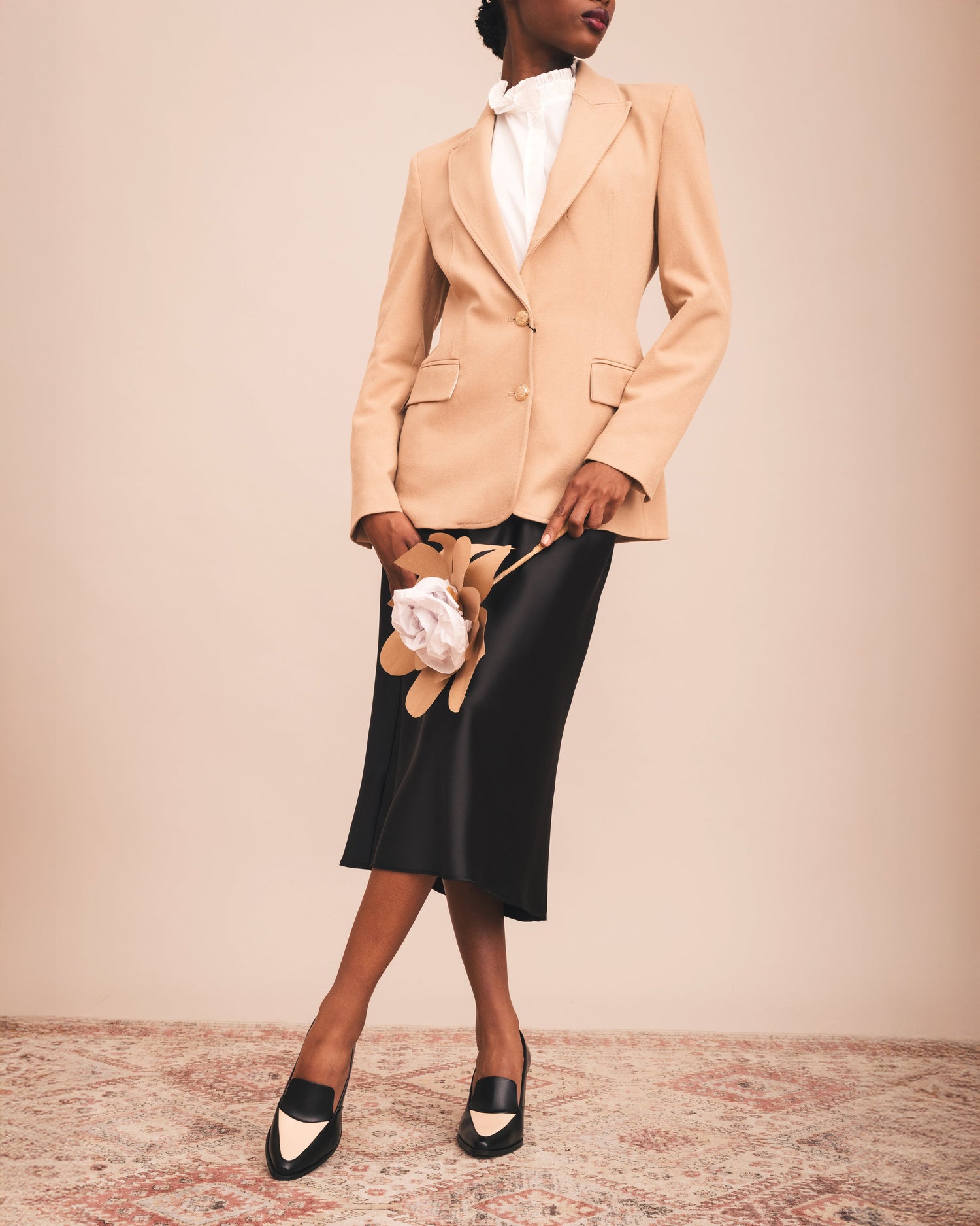 Woman wearing a beige blazer and black skirt with floral design on a beige background