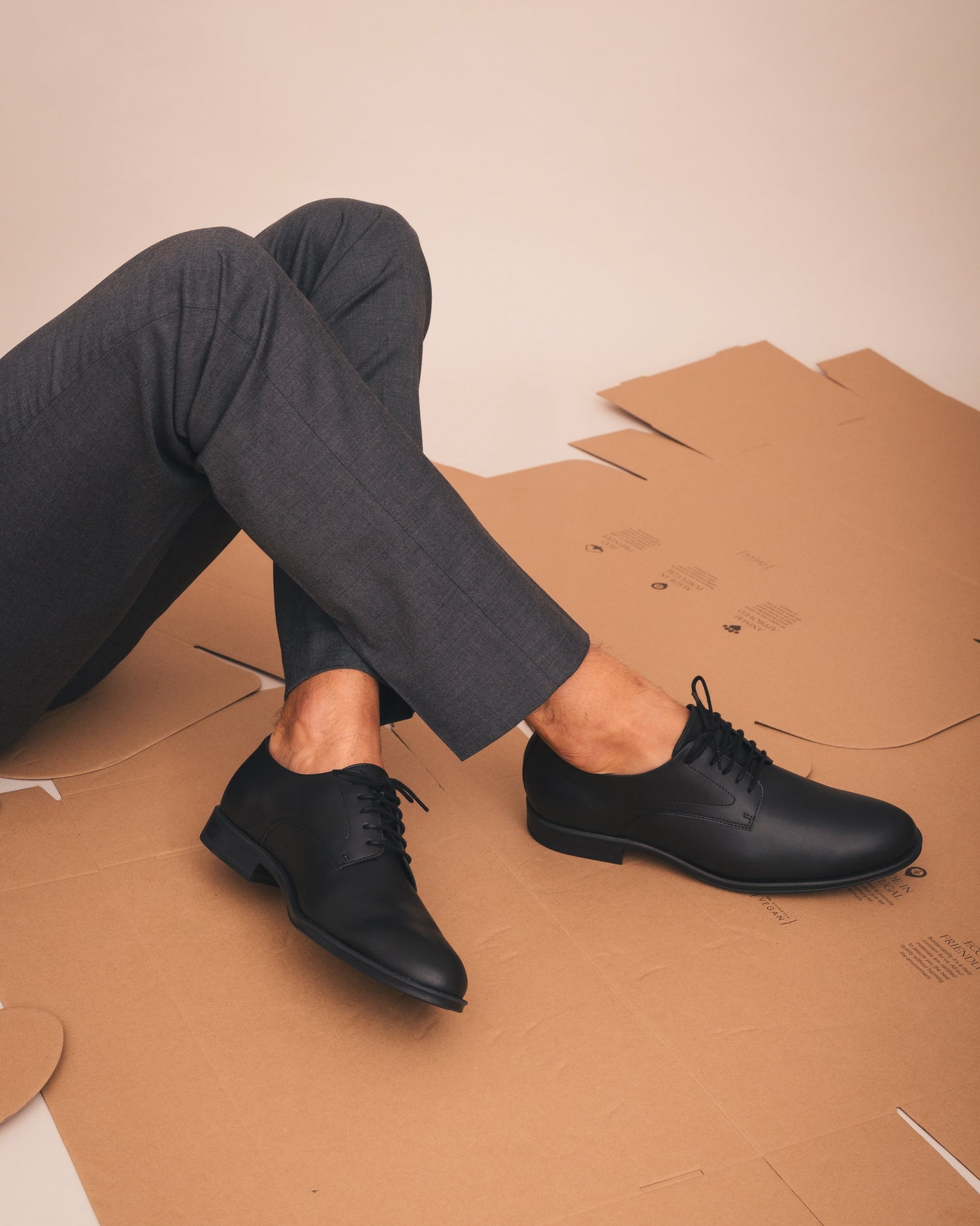 Person wearing black dress shoes sitting on cardboard with a plain background
