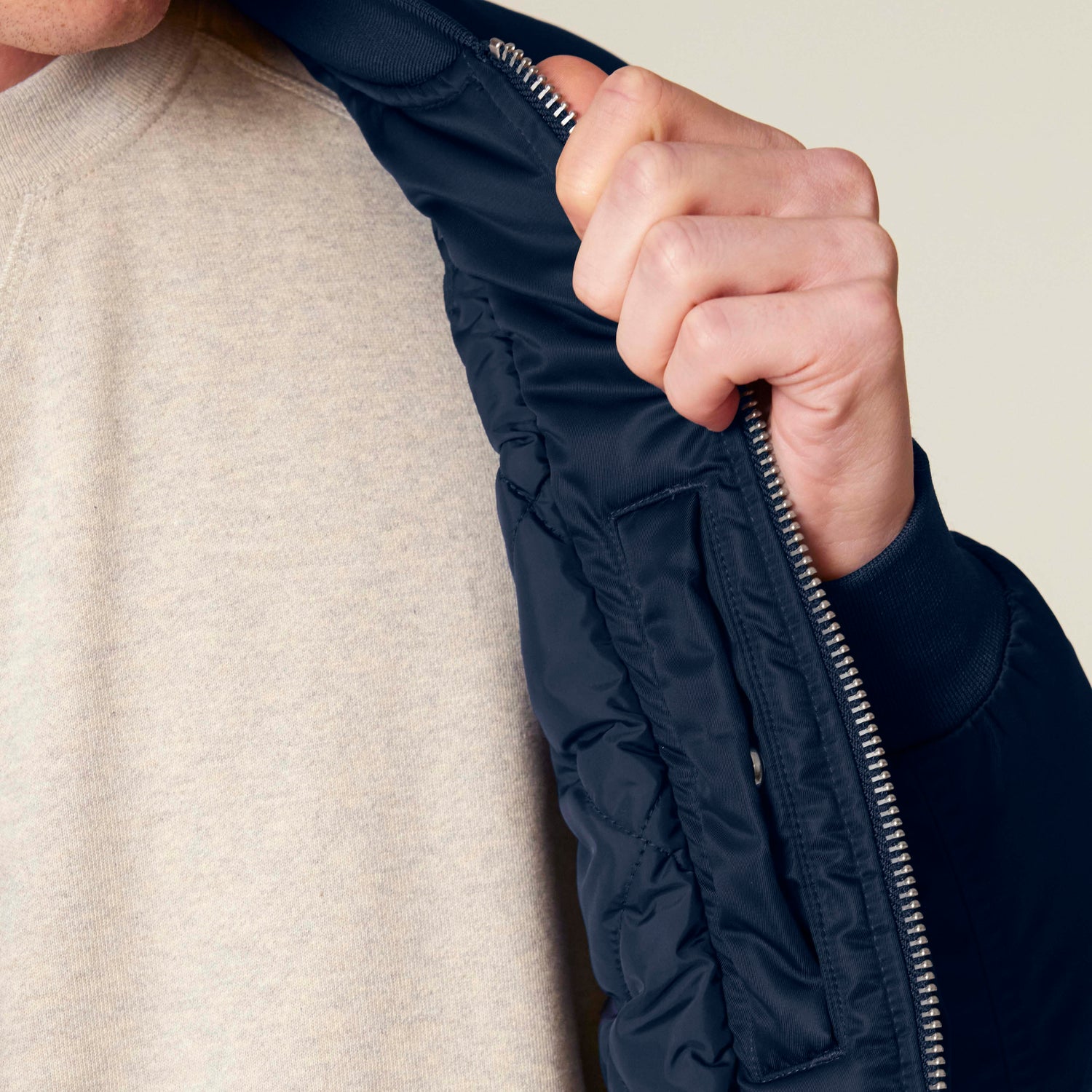 Nahaufnahme einer blauen nachhaltigen Bomberjacke mit gestepptem Innenfutter, Rippbündchen und Metallreißverschluss, GRS-zertifiziert