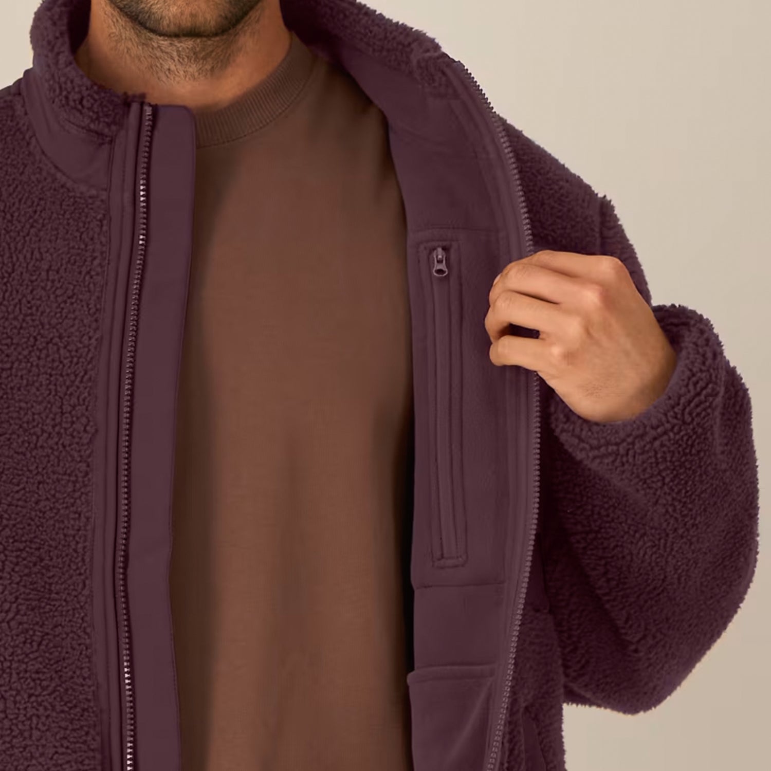 Close-up of a person wearing a sustainable red brown fleece jacket on a neutral background