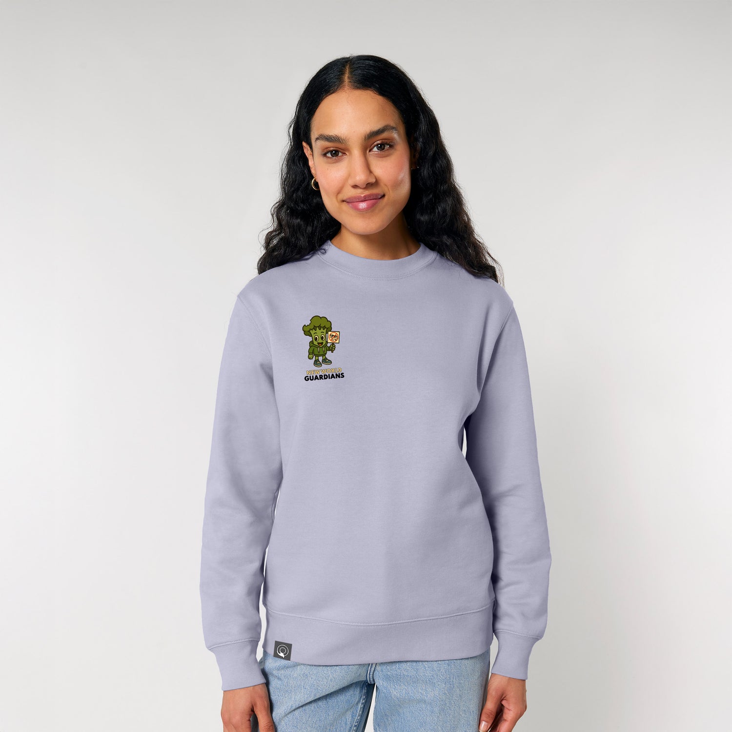 Female model wearing a lavender NEW WORLD GUARDIANS unisex vegan sweater featuring Steamy the broccoli in a comic-style front print and the full Roots for Our Future veggie squad with “Eat Us Not Them” slogan on the back. Made from 100% organic cotton. Conscious vegan fashion and sustainable streetwear in soft pastel tones.