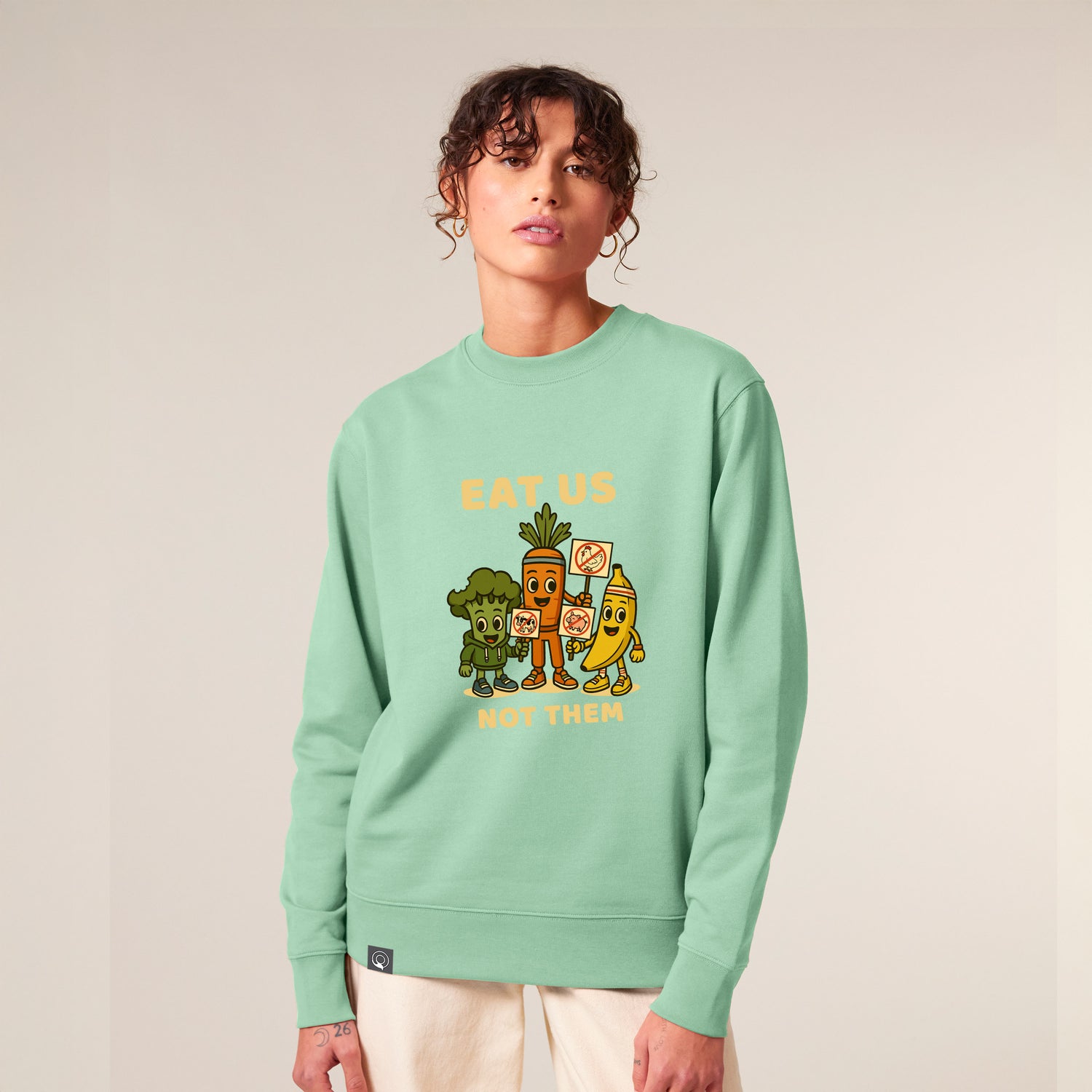 Female model wearing a Misty Jade green NEW WORLD GUARDIANS unisex vegan sweater featuring the full Roots for Our Future veggie squad in a bold comic-style front print with “Eat Us Not Them” slogan. Made from 100% organic cotton. Fresh vegan fashion and sustainable streetwear with expressive character.