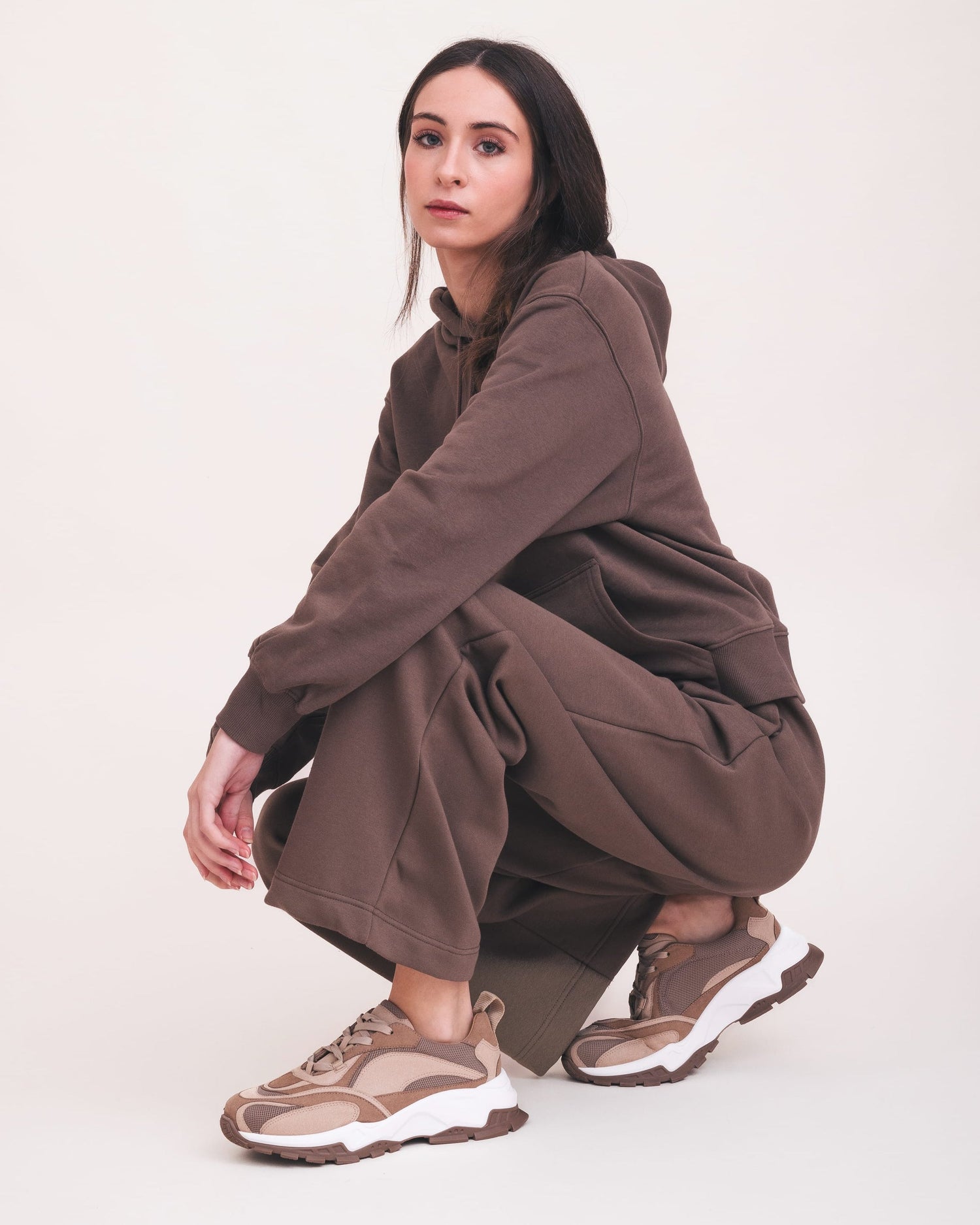 Person wearing a brown outfit with beige sneakers on a white background