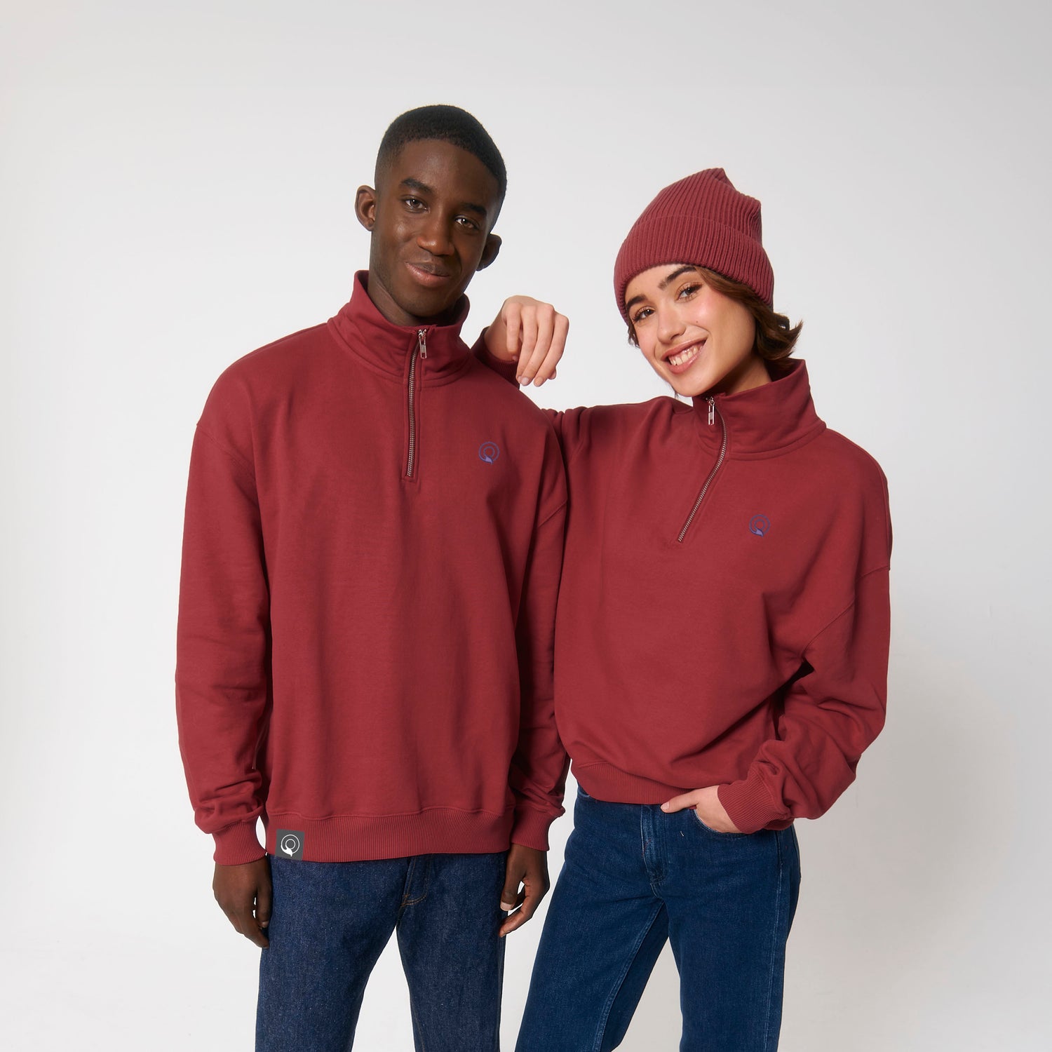 Two models wear red comfortable organic cotton unisex sweaters with herringbone tape zip backing, sustainable quarter-zip design