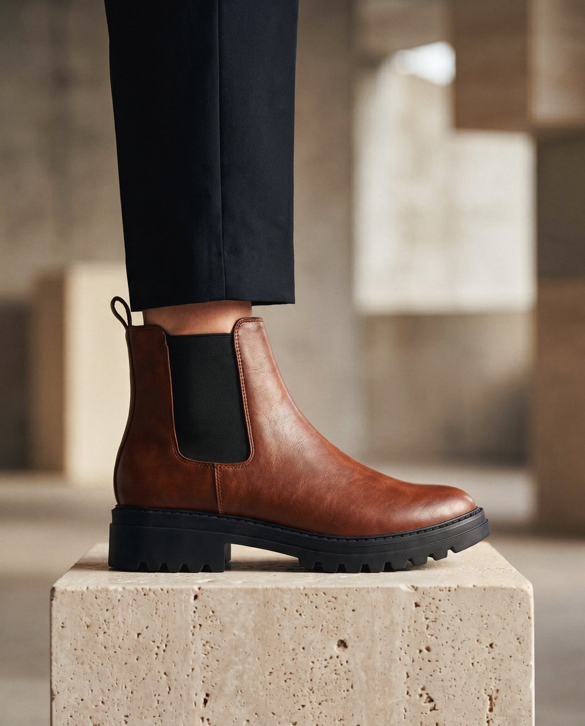 Brauner veganer Lederstiefel mit schwarzer Sohle auf einem Steinblock, verschwommener Hintergrund | NAE Vegan Shoes