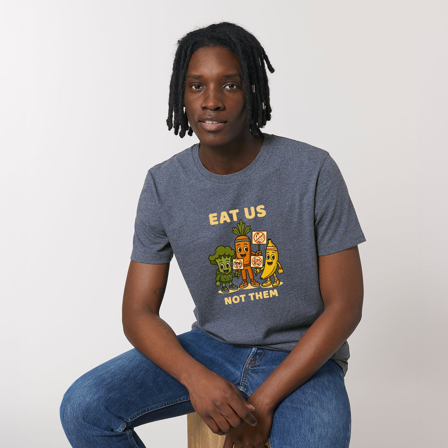 Male model wearing a navy blue NEW WORLD GUARDIANS unisex vegan T-shirt featuring the full Roots for Our Future veggie squad in a large comic-style front print with “Eat Us Not Them” slogan. Made from organic and recycled cotton. Bold vegan fashion and sustainable streetwear with graphic impact.