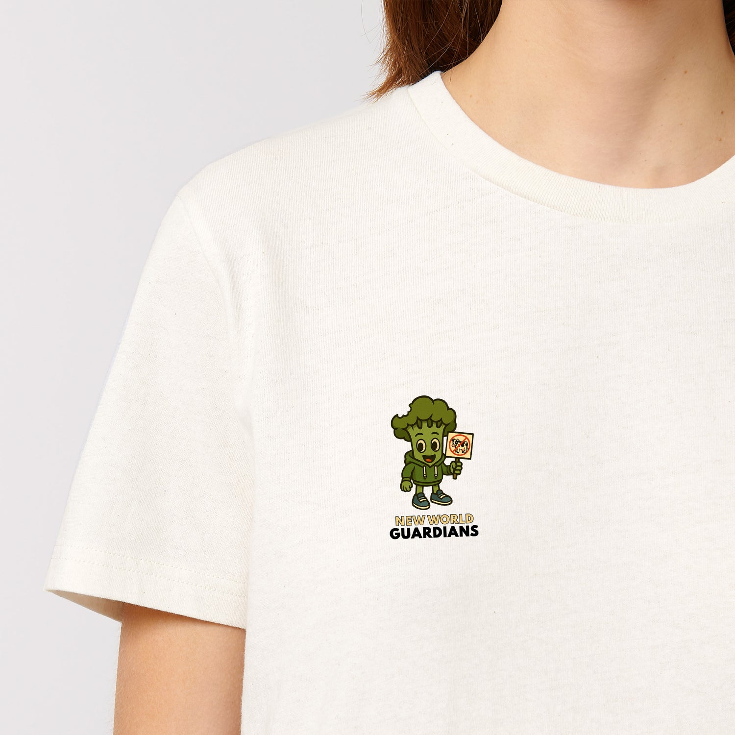 Close-up of female model wearing a white NEW WORLD GUARDIANS unisex vegan T-shirt featuring Steamy the broccoli in a comic-style front print and the full Roots for Our Future veggie squad with “Eat Us Not Them” slogan on the back. Made from organic and recycled cotton. Bold vegan fashion and sustainable streetwear with a message.