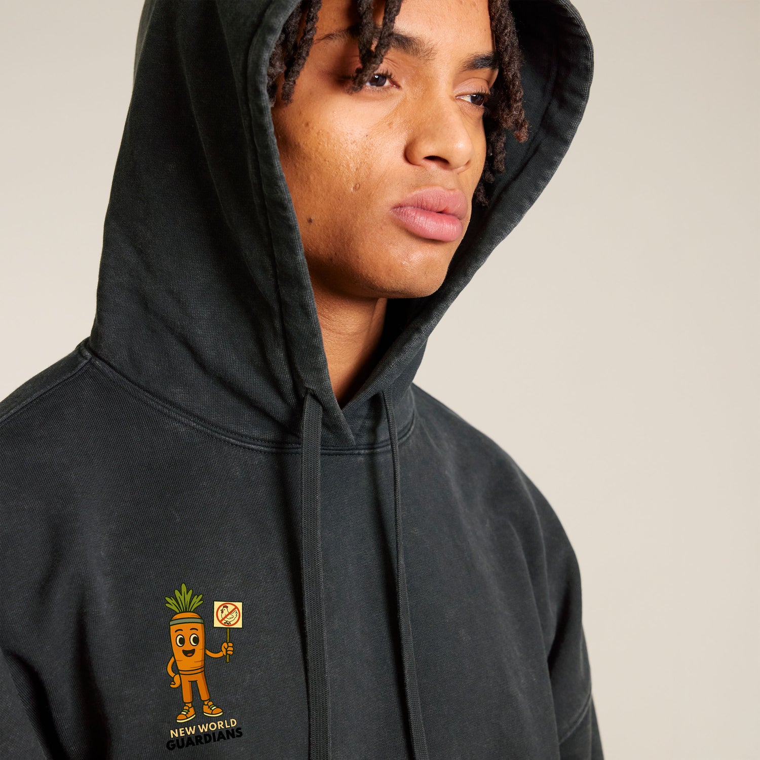 Close-up of a male model wearing a black NEW WORLD GUARDIANS unisex vegan hoodie with hood up, featuring the Roots for Our Future veggie squad comic-style back print and crunch print on the front. Made from 100% organic cotton. Bold vegan fashion meets sustainable streetwear.