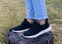 A woman in black and white Explorer V2 hemp shoes for women, stands on an old tree stump.