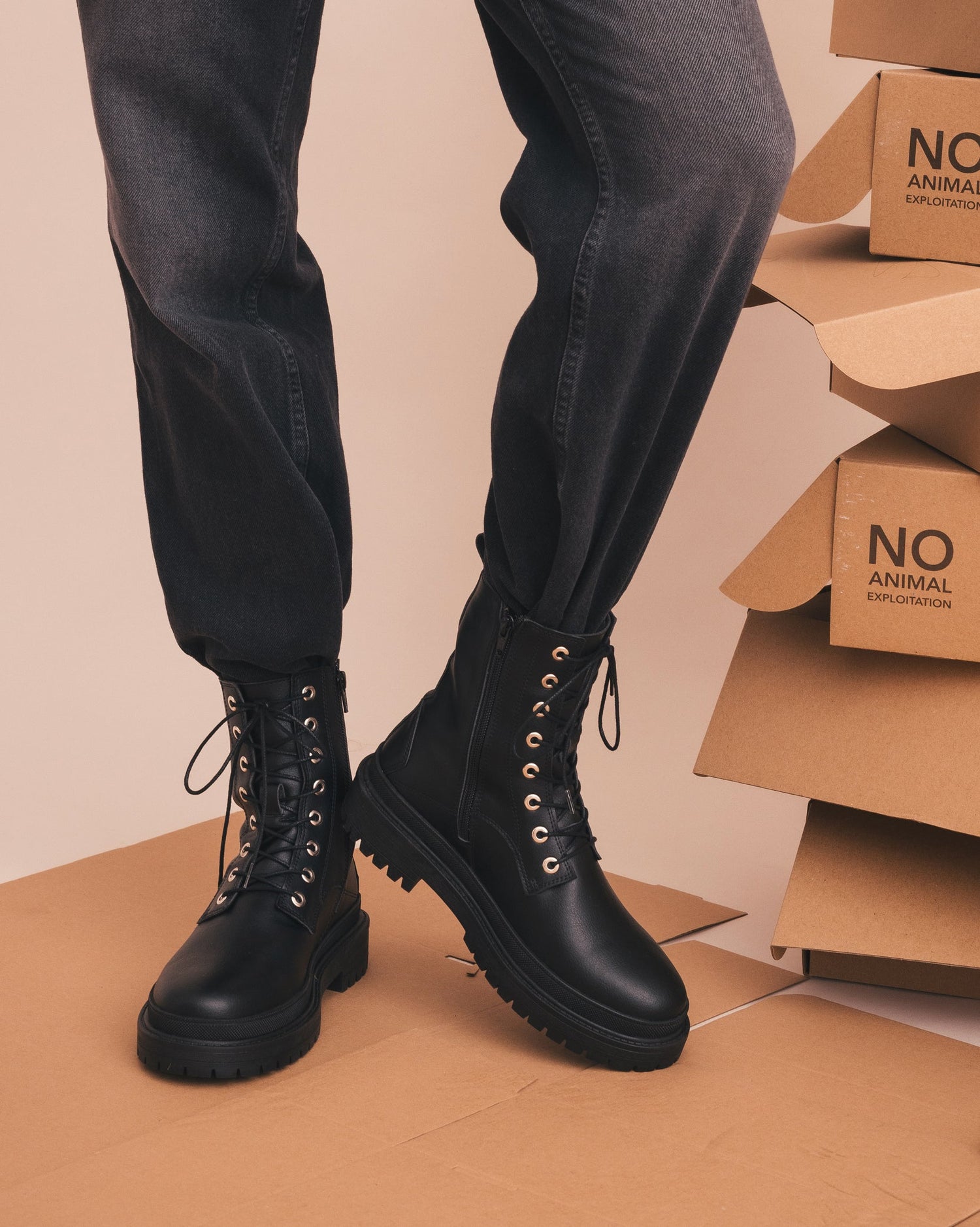 Person wearing black leather boots with stacked cardboard boxes in the background
