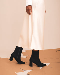 Black ankle boots worn with a white dress on a beige background