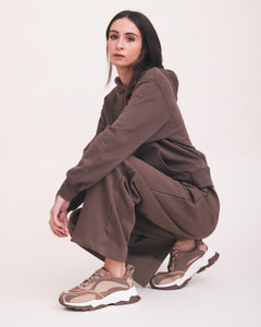 Person wearing a brown outfit with beige sneakers on a white background