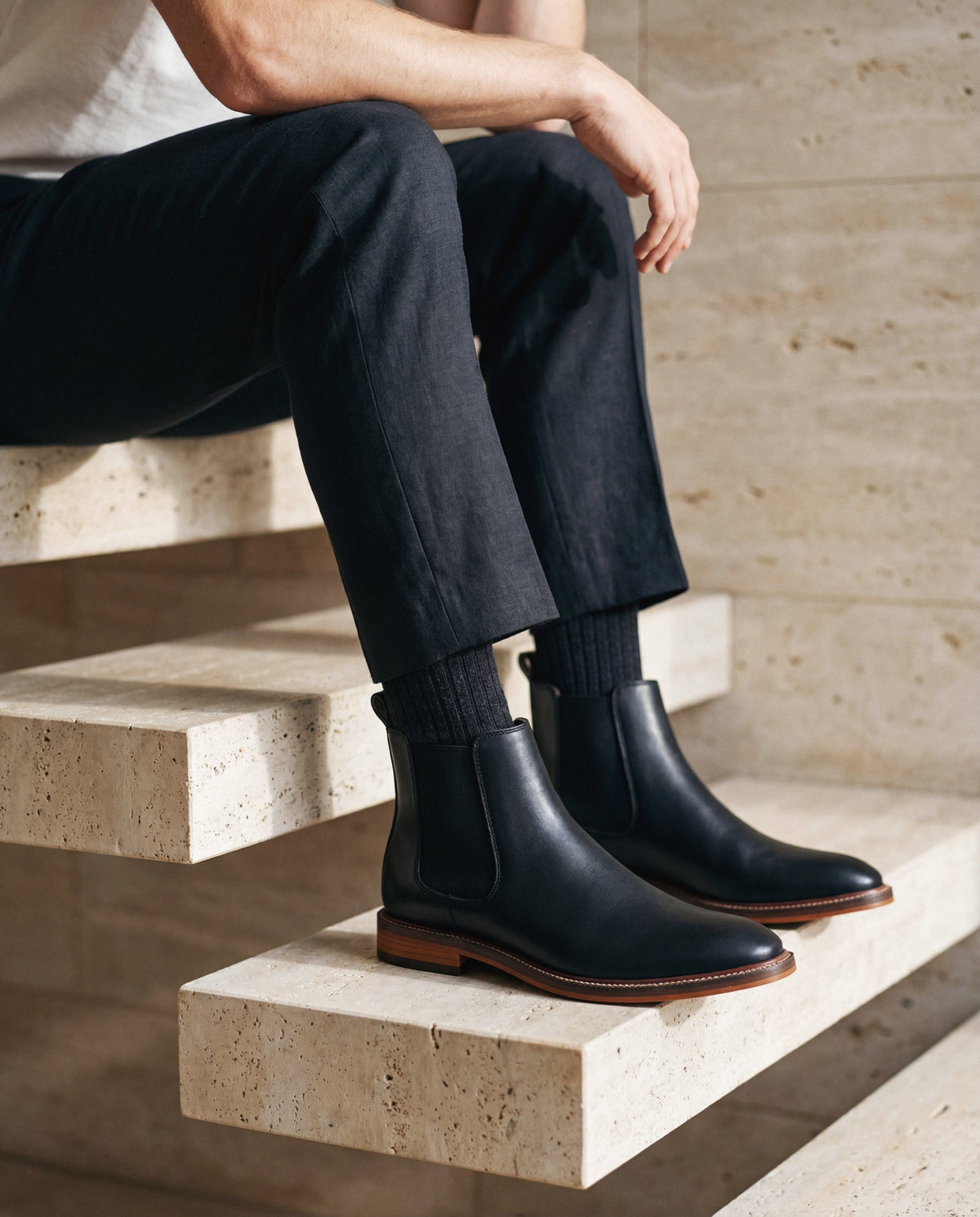 Person, die schwarze vegane Lederstiefel trägt, sitzt auf Steinstufen
