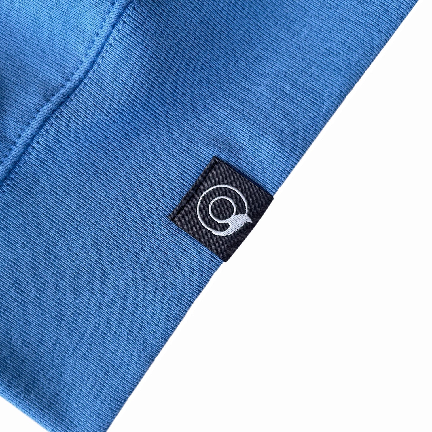 Close-up of a blue NEW WORLD GUARDIANS Sweater with a brand logo tag on a white background