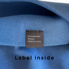 Close-up of a blue NEW WORLD GUARDIANS Sweater with a label indicating sustainability, veganism, and cruelty-free practices.