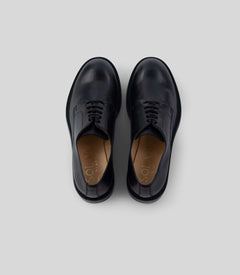 Vegan Derby - Woman in black leather, featuring an open lacing system, perfect for formal and casual events.