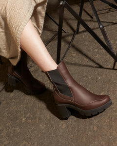 Brown vegan ankle boots worn by a person sitting on a bench.